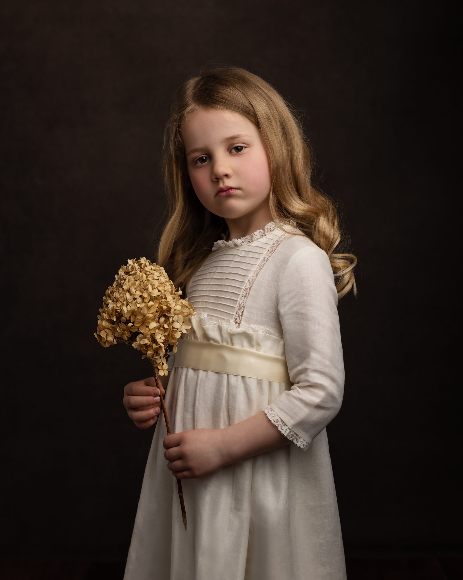 Blond hair little girl in a vintage cream dress holding a dried flower during her Fine Art Photoshoot with Alison McKenny Photography
