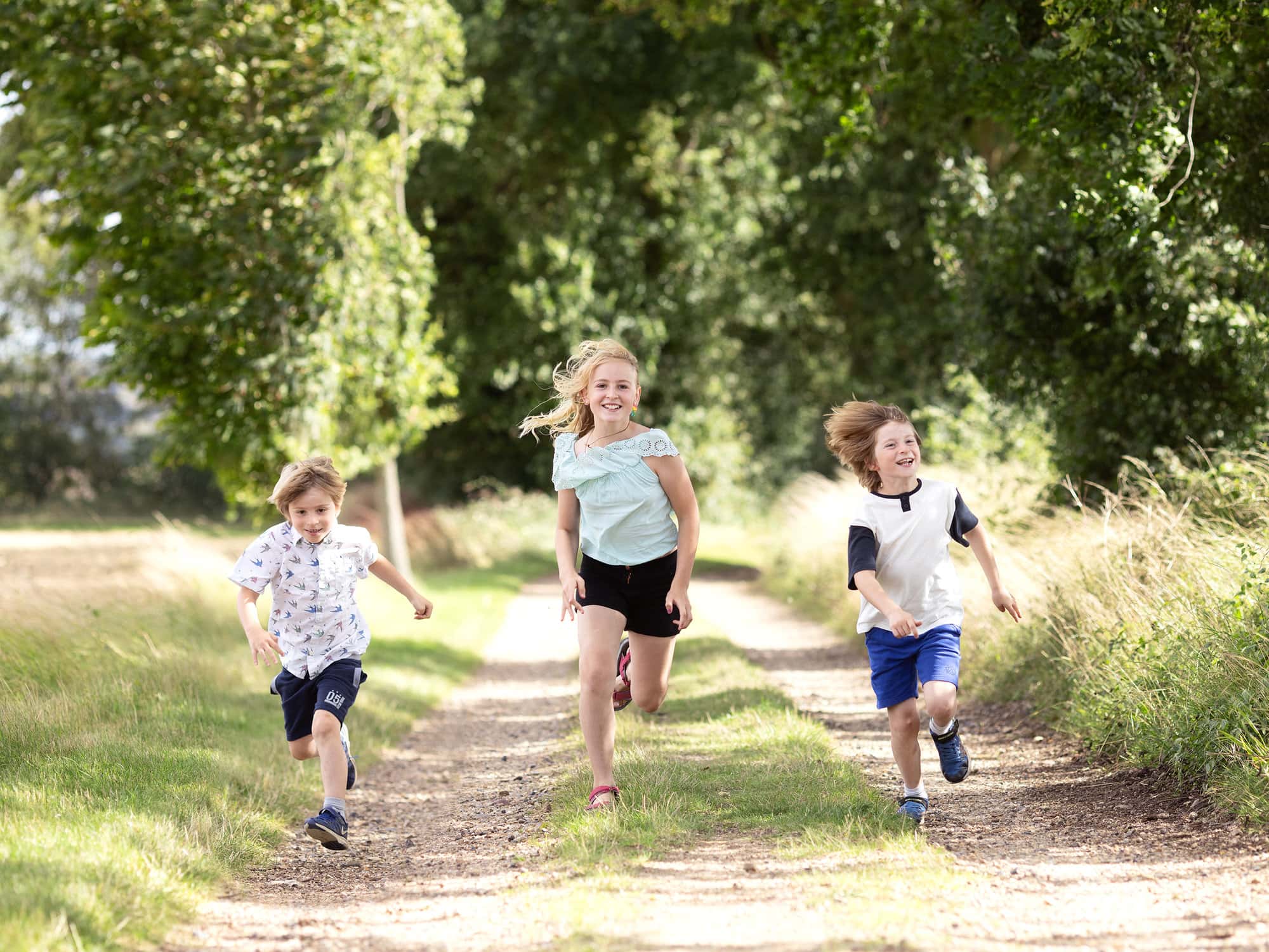 3 children racing each other down a country track during a family photoshoot with Alison McKenny Photography