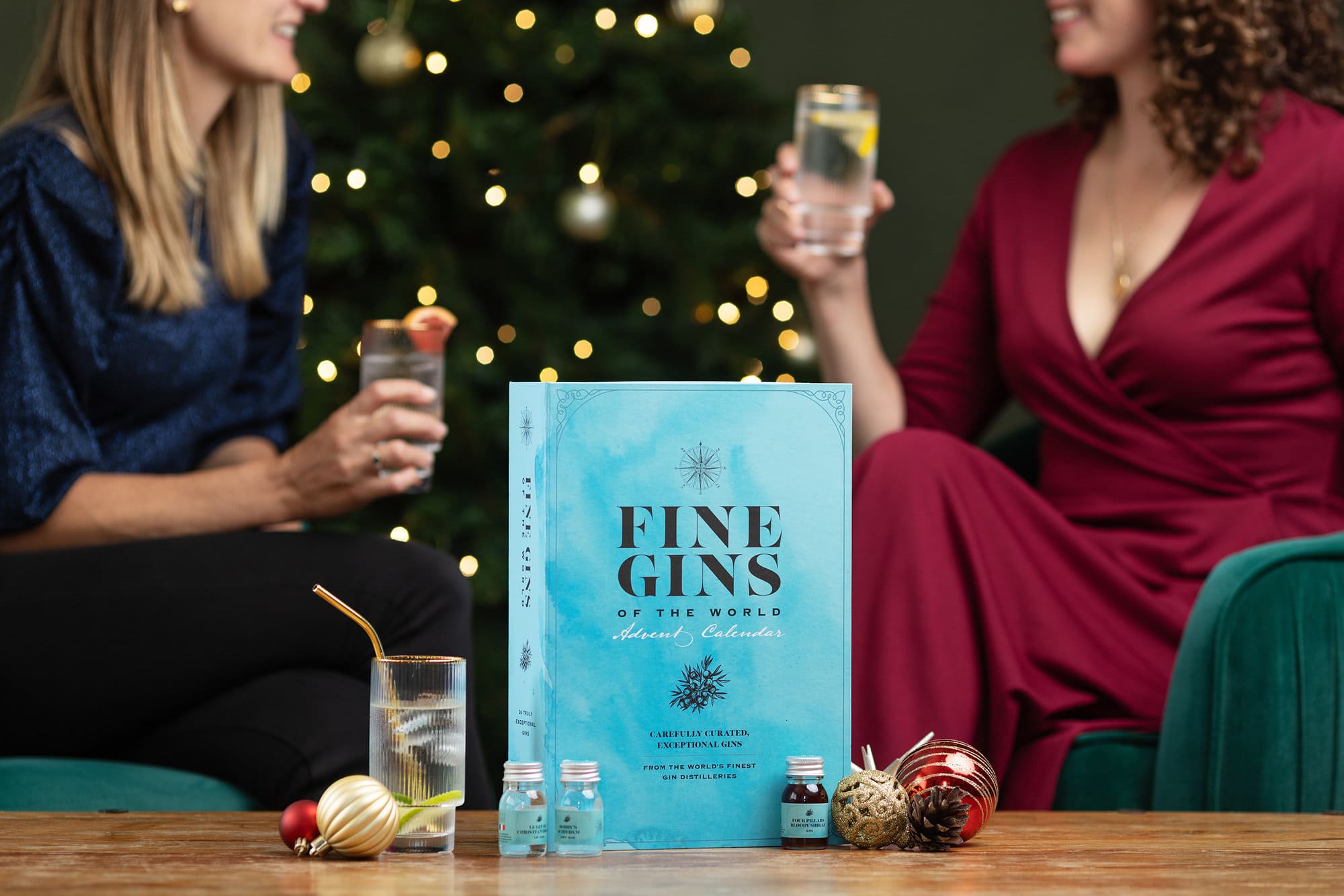 Spirit Co. Fine Gin Advent Calendar sitting on a coffee table with two models holding glasses in the background
